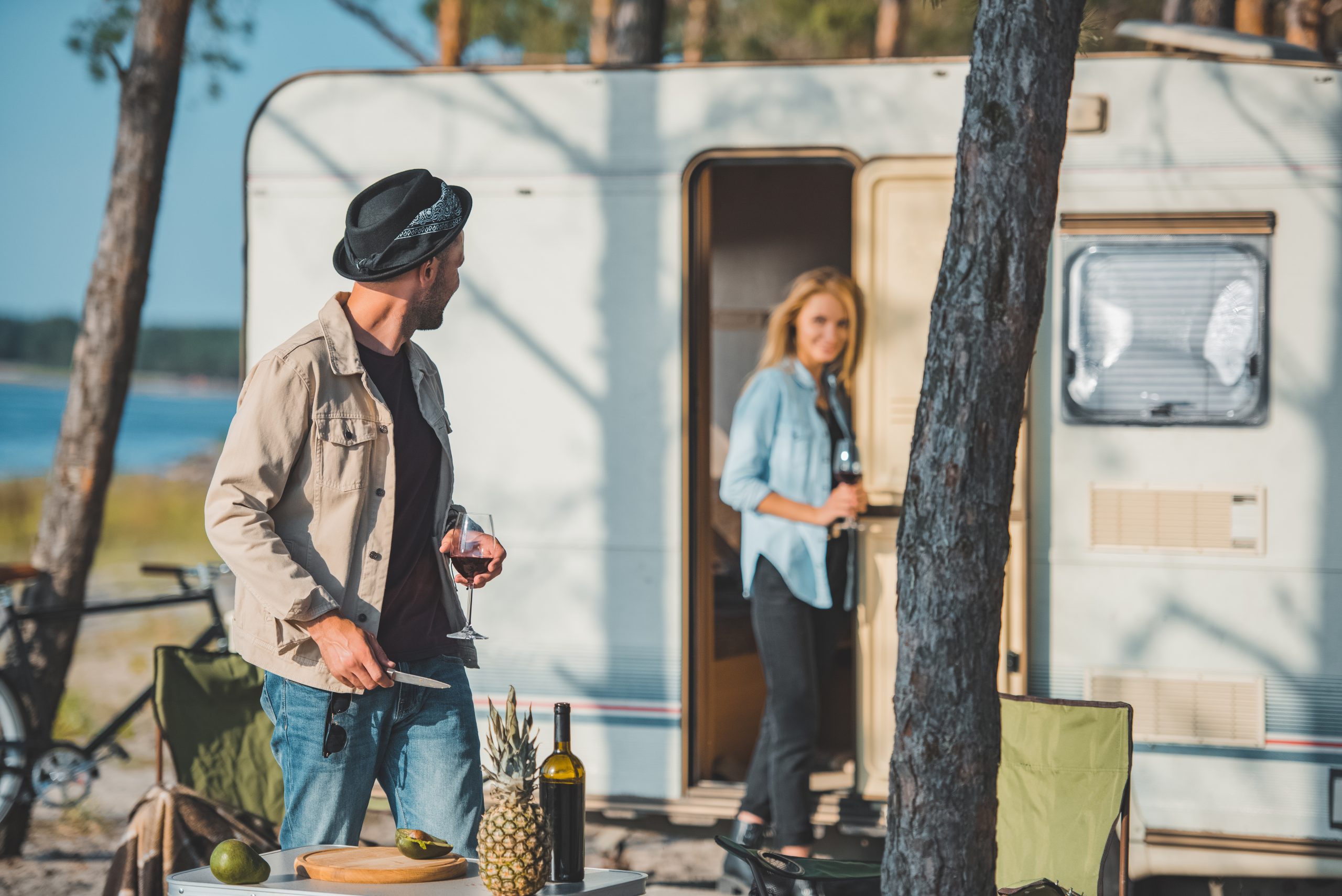 selective focus of handsome man with glass of wine looking at girlfriend near trailer